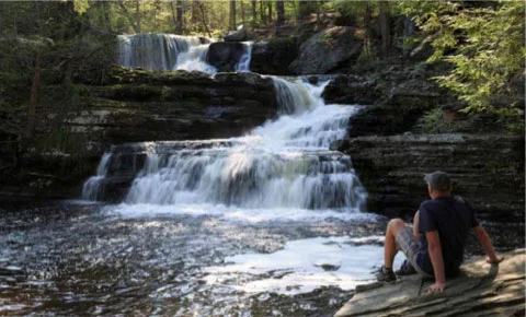 Man sits watching a waterfall