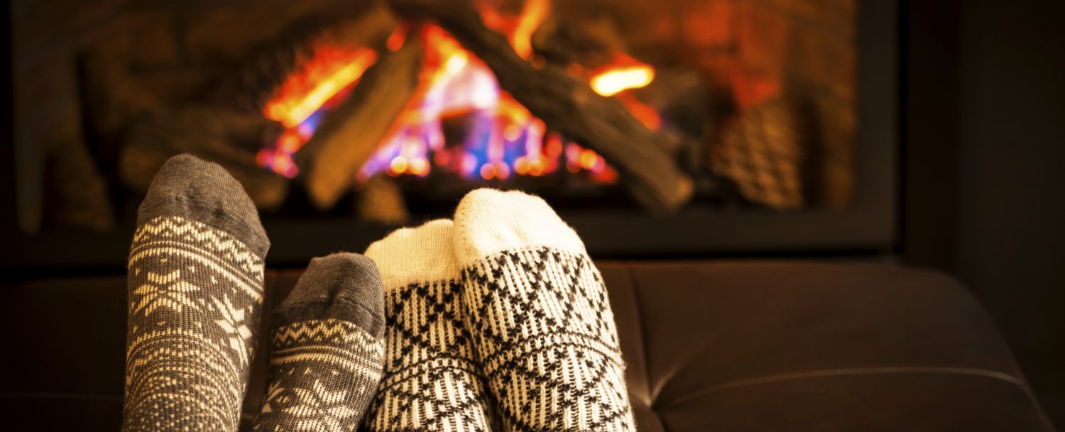 2 pair of feet in cozy socks warming up by a roaring fire